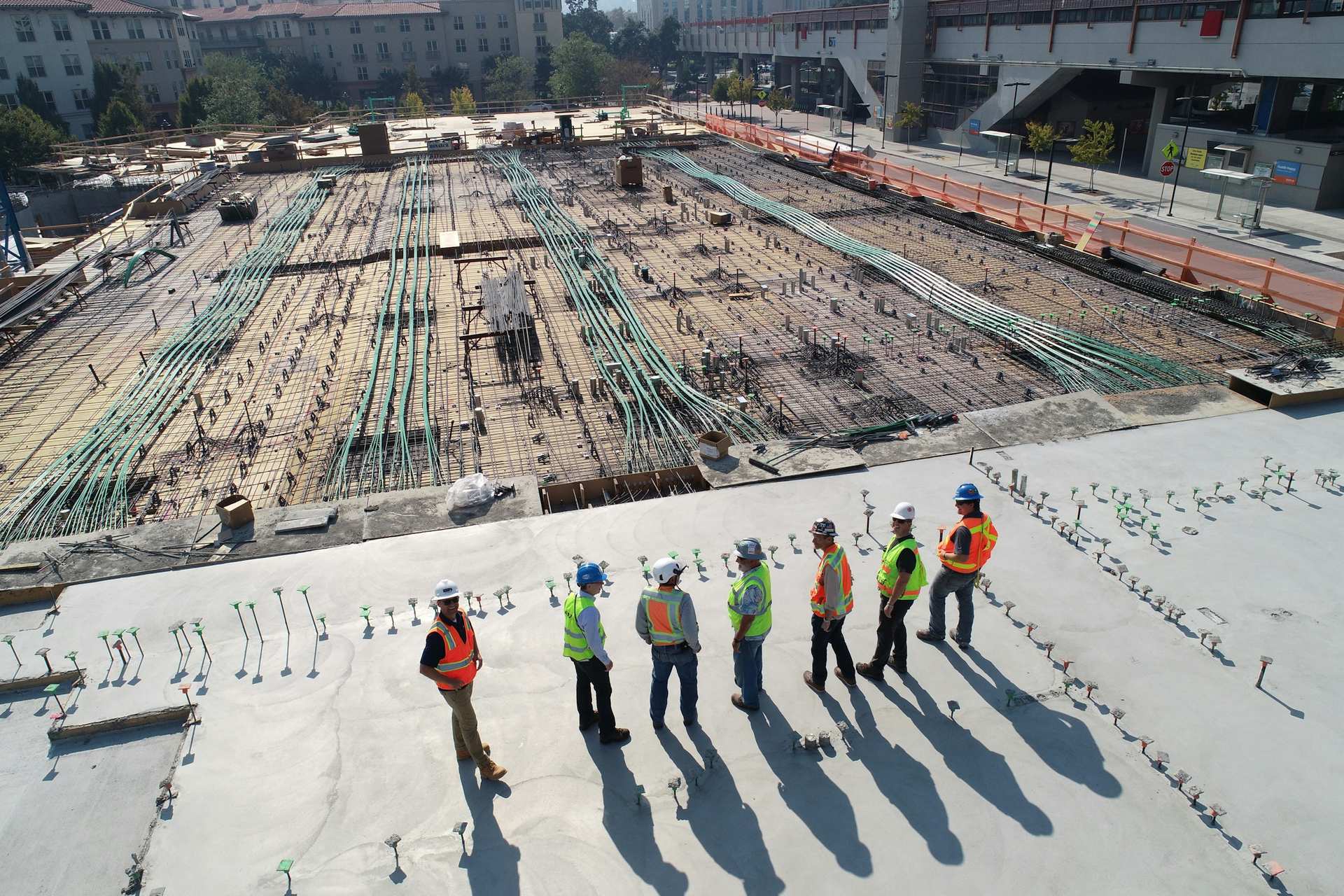 A construction crew standing on a freshly poured concrete deck above a rebar-laid foundation.
